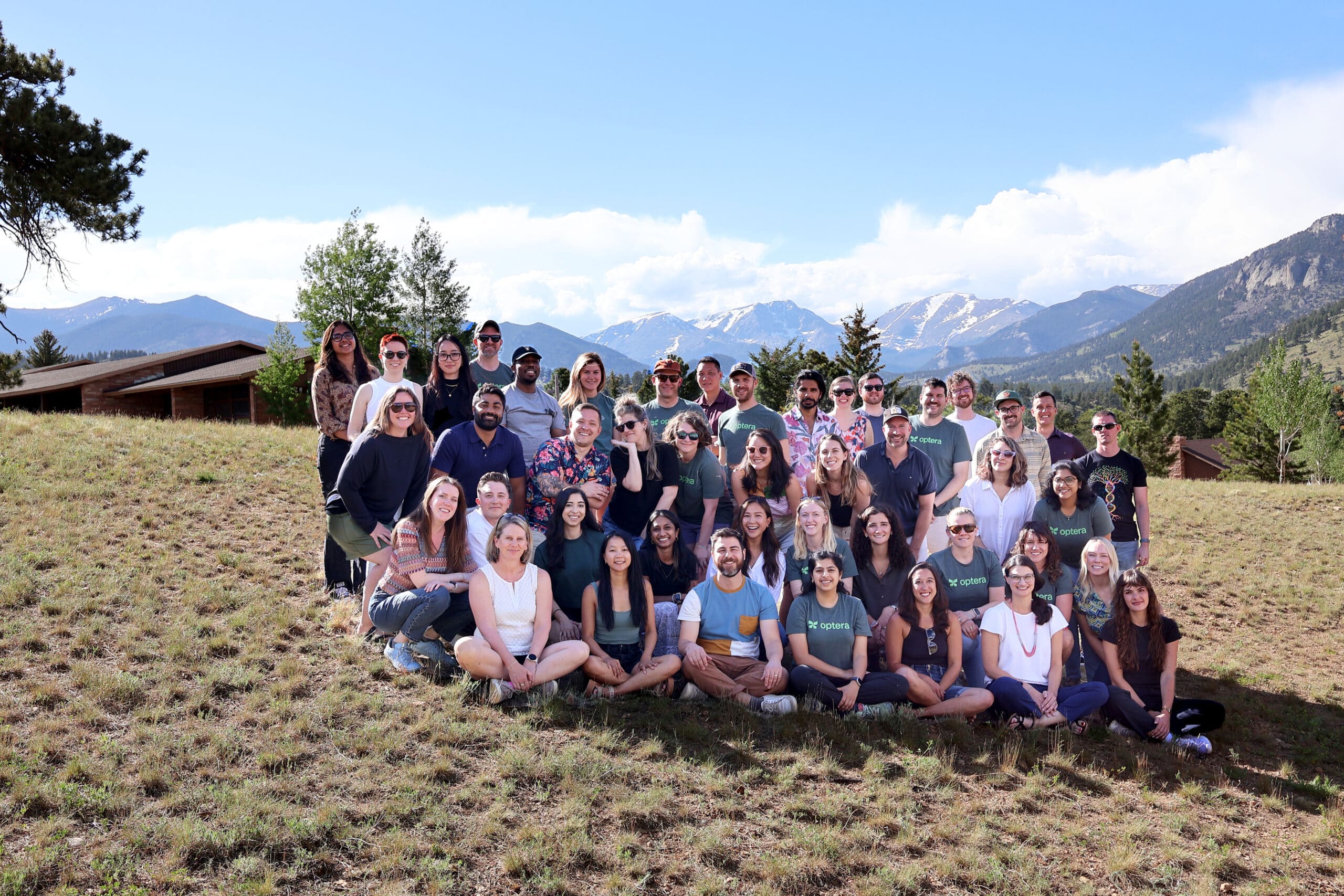 The Optera team poses in a group on a sunny day in front of an epic mountain range